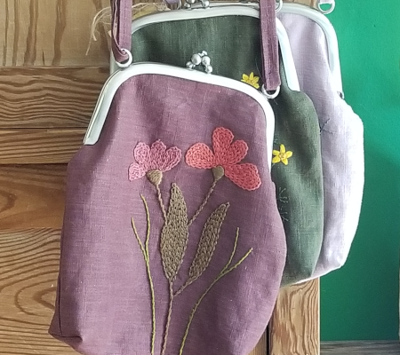 Handtasche Cosmea flaumenfarbene Handtasche vor zwei weiteren hängend mit aufgesticktem Blumenmotiv